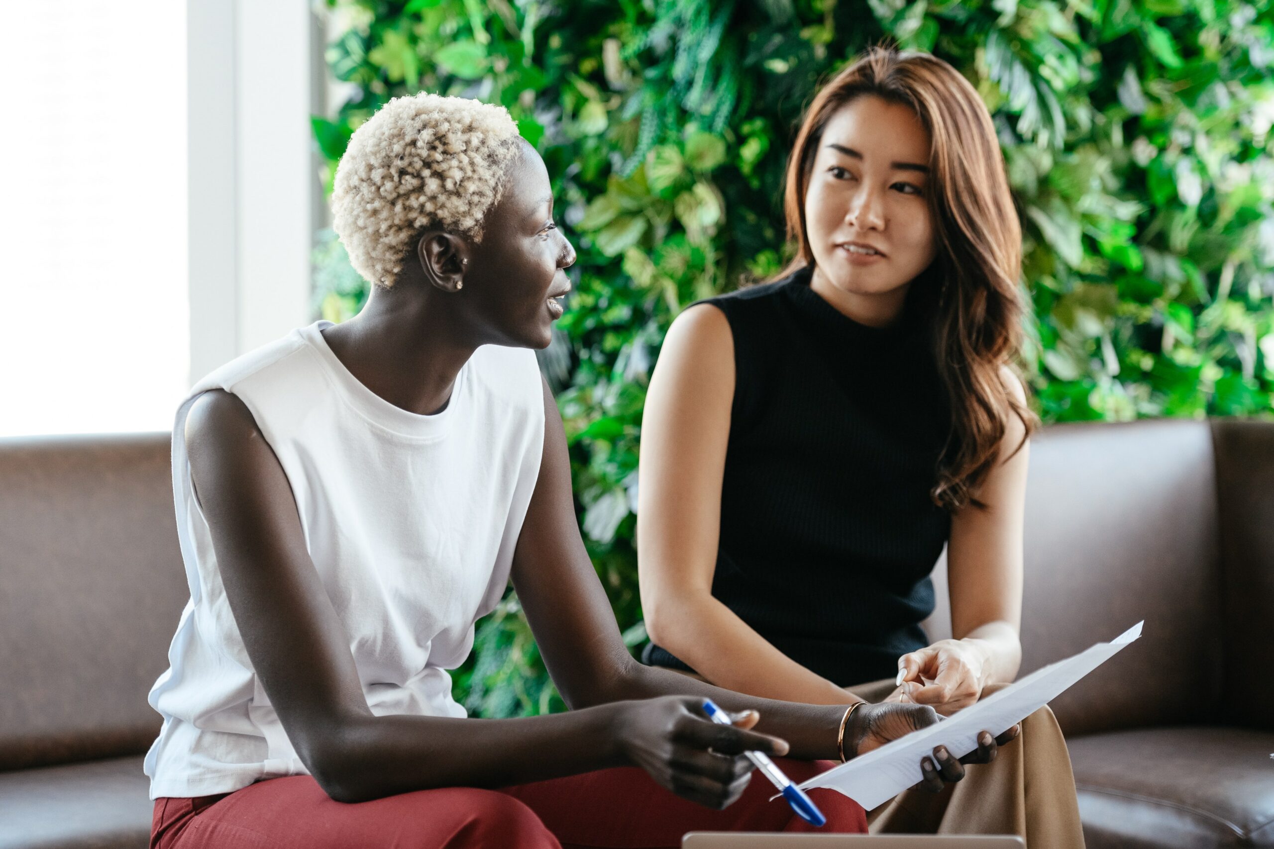 Two women sitting beside and looking at each other with work documents in hand